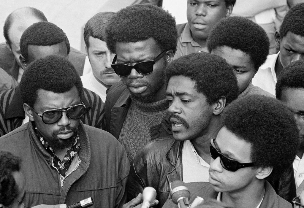 Bobby Seale, right, chairman of the Black Panther Party, is one of three speakers at a sidewalk news conference in Oakland, Ca., Nov. 21, 1968. The other speakers are Ben Stewart, left, head of the Black Students organization at San Francisco State, and George Murray, center dark glasses, suspended teacher at State. (AP Photo/Ernest K. Bennett)